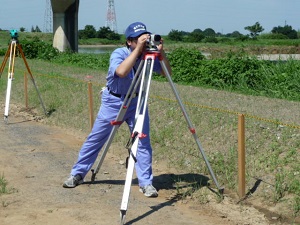 測量機器（レベル）を使って地面の高さを測っています。